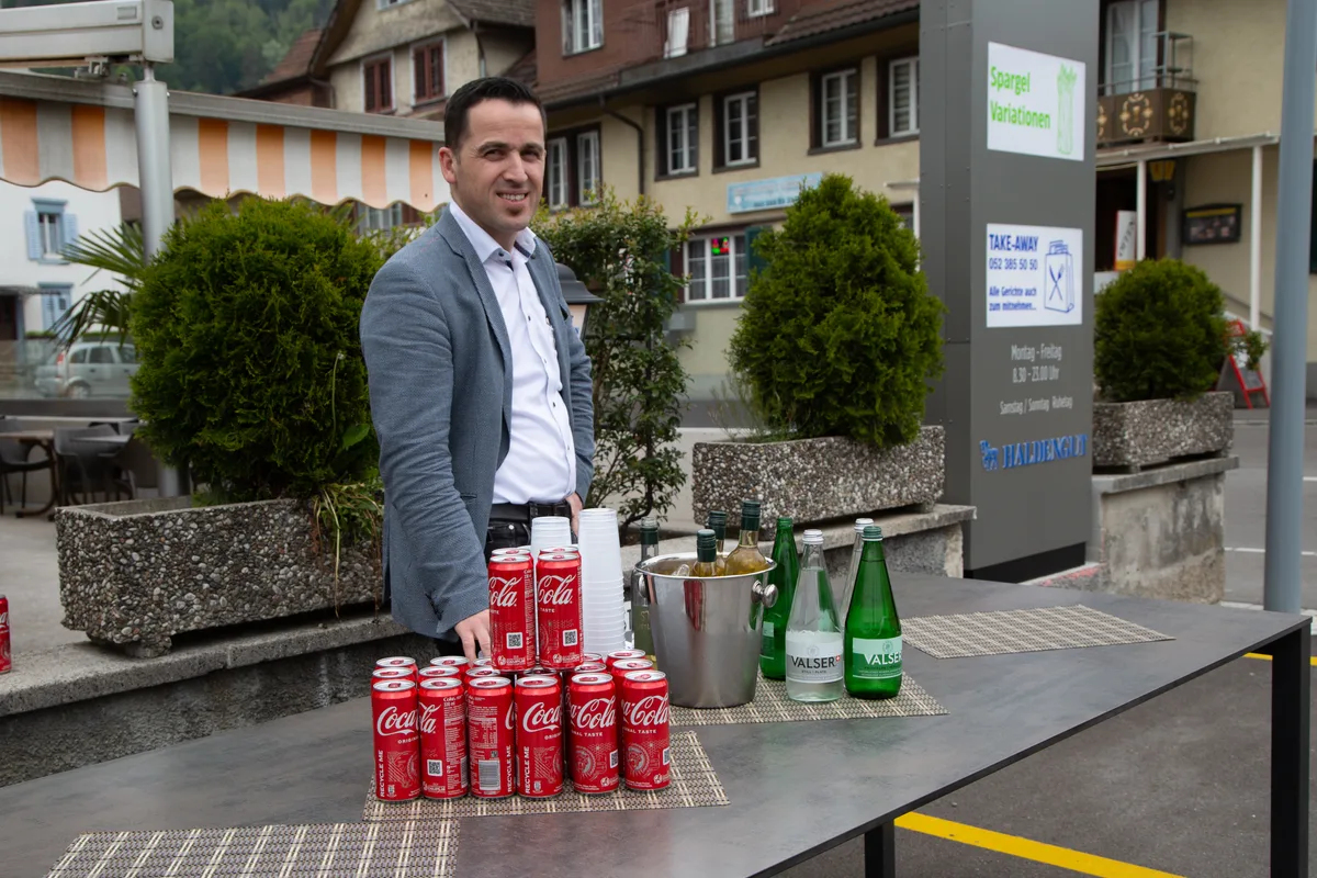 Wirt Vesel Veseli vom «Landenberg» schenkt den Apéro aus. Man sieht einen Mann an einem Tisch voller Getränke.